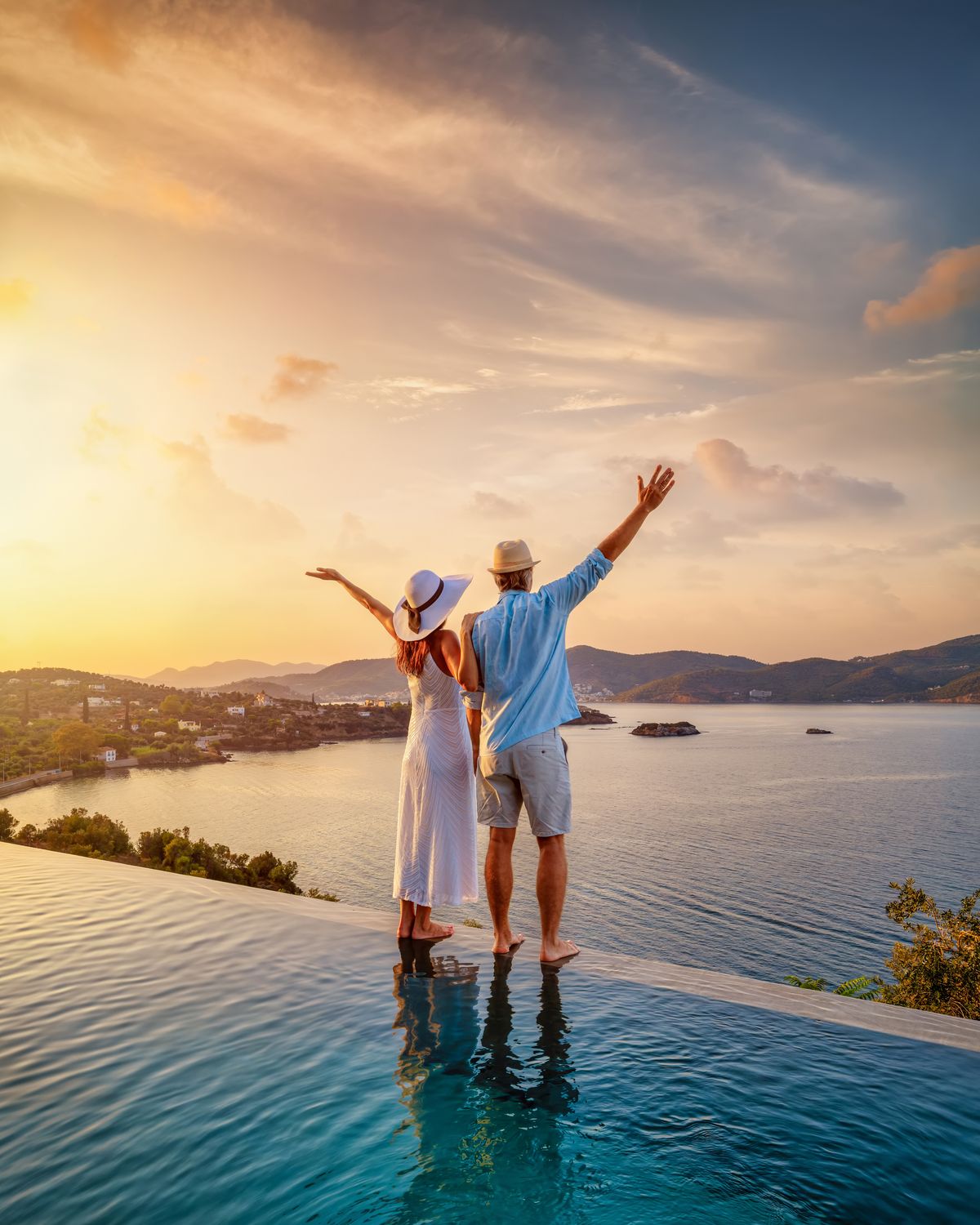 Casal à beira de uma piscina de borda infinita ao pôr do sol, com vista para o mar
