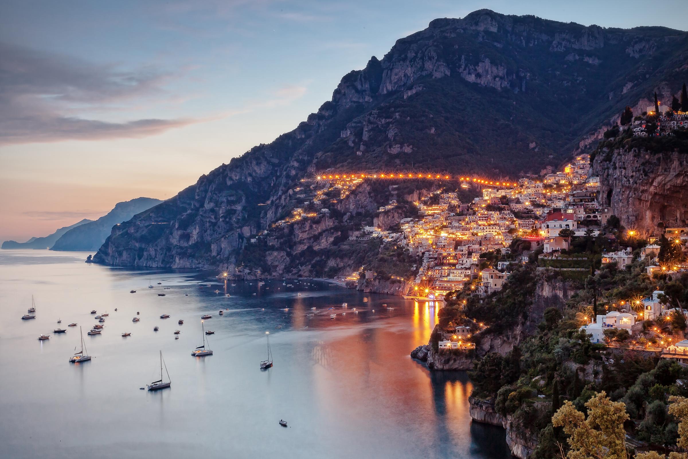 Positano iluminada ao entardecer, com as casas na encosta, o mar e as montanhas da Costa Amalfitana